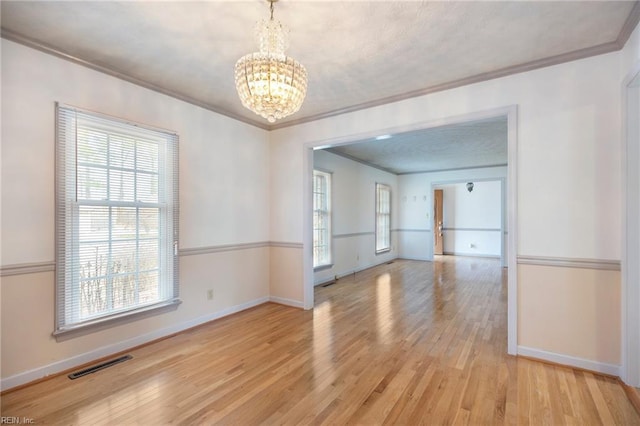 spare room with visible vents, crown molding, light wood finished floors, and an inviting chandelier