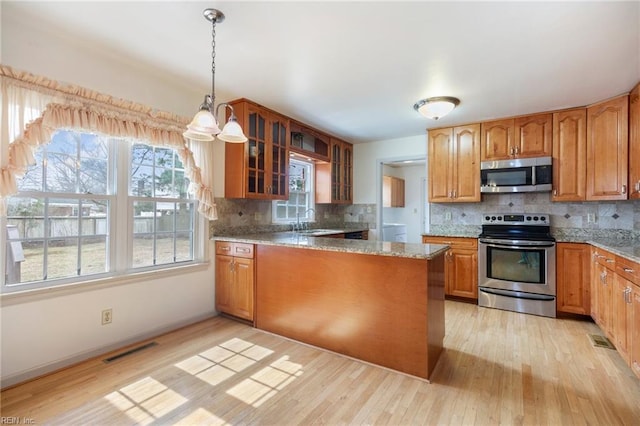 kitchen with light wood finished floors, visible vents, glass insert cabinets, appliances with stainless steel finishes, and a sink