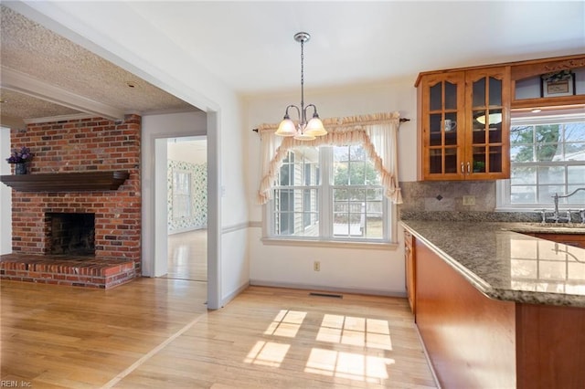 kitchen featuring light wood-type flooring, a brick fireplace, beam ceiling, brown cabinetry, and glass insert cabinets