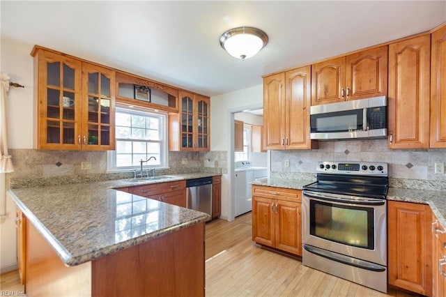 kitchen with stainless steel appliances, a peninsula, a sink, light stone countertops, and glass insert cabinets