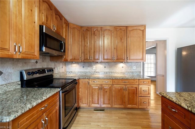 kitchen featuring light wood finished floors, visible vents, decorative backsplash, light stone counters, and stainless steel appliances