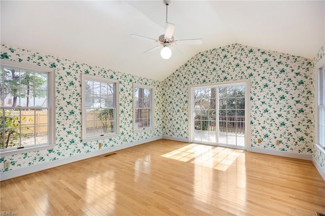 unfurnished room featuring light wood-style floors, lofted ceiling, a healthy amount of sunlight, and wallpapered walls