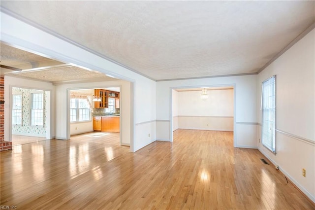 unfurnished living room featuring a textured ceiling, visible vents, baseboards, light wood-type flooring, and crown molding