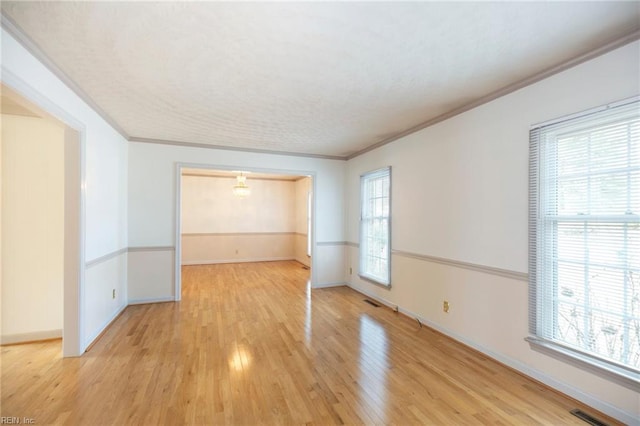 unfurnished room with light wood-style floors, visible vents, ornamental molding, and baseboards