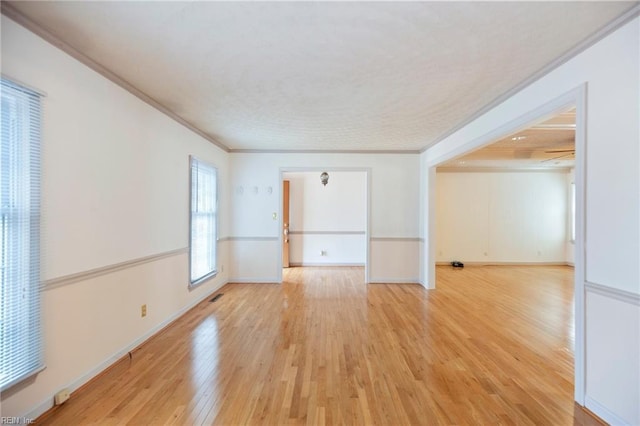 empty room with light wood finished floors, baseboards, visible vents, and crown molding