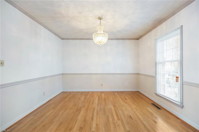 spare room featuring visible vents, crown molding, an inviting chandelier, and wood finished floors