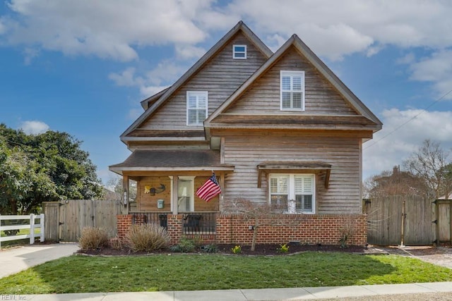 view of front of property featuring a gate, a porch, fence, and a front lawn