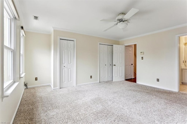 unfurnished bedroom with multiple closets, visible vents, crown molding, and carpet floors