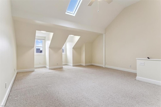 additional living space featuring vaulted ceiling with skylight, a ceiling fan, and light colored carpet