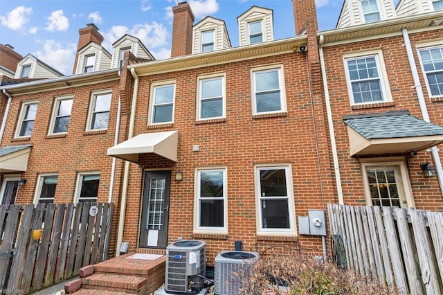 view of front of home featuring brick siding, fence, a chimney, and central AC unit