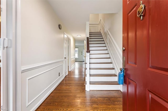 foyer entrance featuring stairs, a decorative wall, and wood finished floors