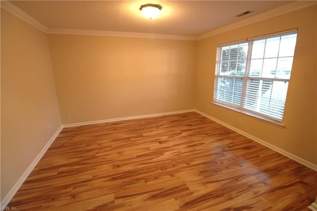 empty room with a textured ceiling, wood finished floors, visible vents, baseboards, and crown molding