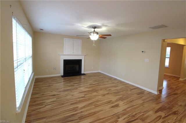 unfurnished living room with baseboards, a fireplace with flush hearth, visible vents, and light wood-style floors