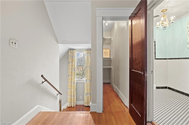 corridor with wood finished floors, baseboards, lofted ceiling, a notable chandelier, and an upstairs landing