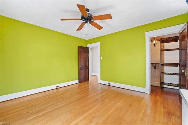 unfurnished bedroom with a spacious closet, wood finished floors, and baseboards