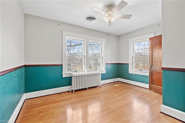 unfurnished room with visible vents, wood finished floors, radiator heating unit, baseboards, and ceiling fan