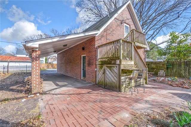 view of property exterior featuring decorative driveway, an attached carport, fence, stairway, and brick siding