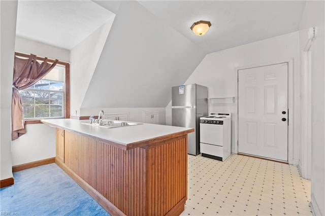 kitchen featuring lofted ceiling, a peninsula, freestanding refrigerator, white range, and a sink