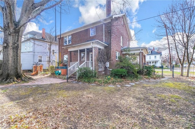 rear view of property featuring brick siding, covered porch, a chimney, and fence