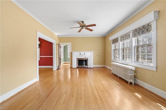 unfurnished living room with a fireplace with flush hearth, radiator, light wood-style flooring, and crown molding