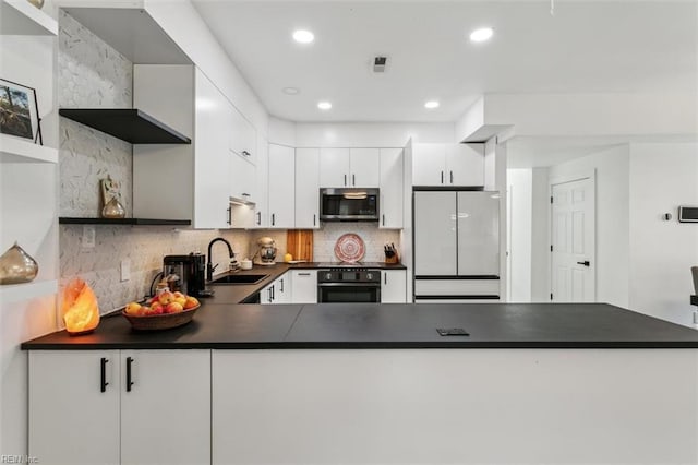 kitchen featuring dark countertops, stainless steel microwave, oven, freestanding refrigerator, and a sink