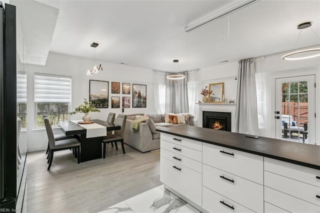 kitchen with dark countertops, open floor plan, a warm lit fireplace, hanging light fixtures, and white cabinets