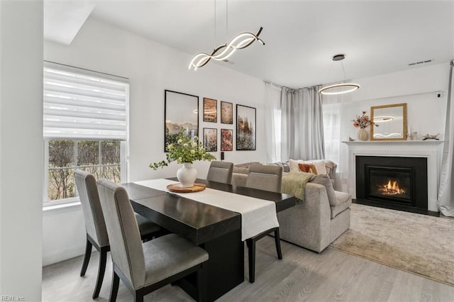 dining room featuring wood finished floors, visible vents, baseboards, a glass covered fireplace, and a notable chandelier