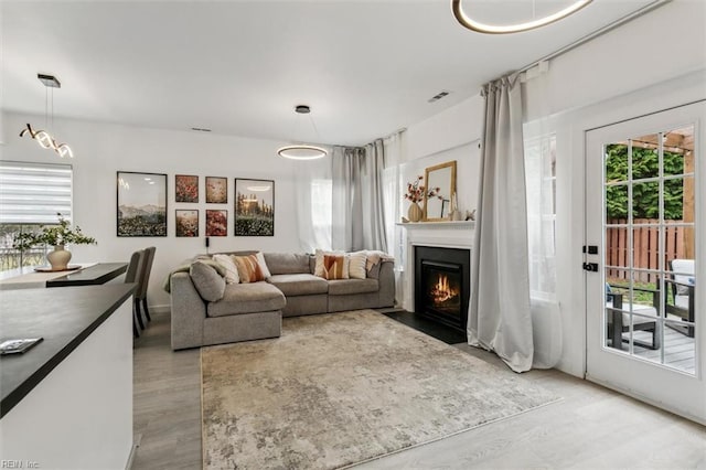 living area with visible vents, a fireplace with flush hearth, and light wood-style floors