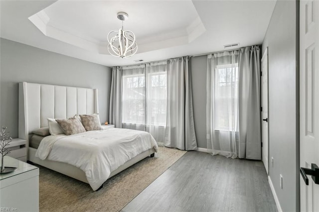 bedroom featuring visible vents, ornamental molding, a tray ceiling, wood finished floors, and a chandelier