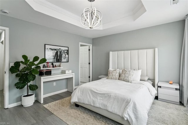 bedroom with wood finished floors, baseboards, ornamental molding, a raised ceiling, and a chandelier