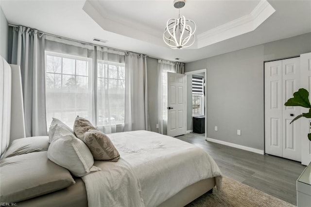 bedroom with a tray ceiling, visible vents, wood finished floors, and ornamental molding