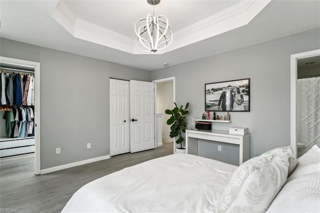 bedroom featuring wood finished floors, baseboards, a tray ceiling, ornamental molding, and multiple closets