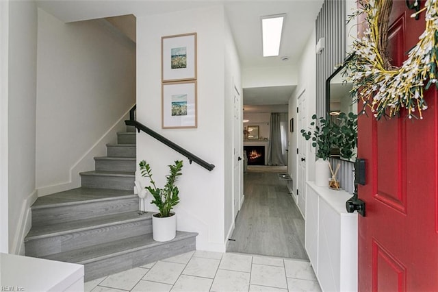 foyer entrance with baseboards, a warm lit fireplace, and stairs