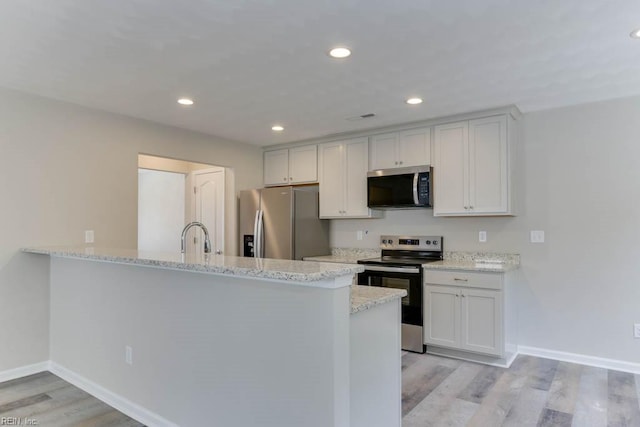 kitchen featuring stainless steel appliances, light wood-style flooring, a sink, light stone countertops, and baseboards