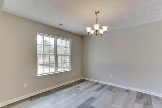 empty room with baseboards, wood finished floors, visible vents, and an inviting chandelier