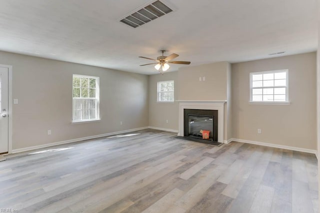 unfurnished living room featuring light wood-style floors, a fireplace with flush hearth, visible vents, and baseboards