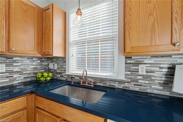 kitchen featuring hanging light fixtures, backsplash, dark countertops, and a sink