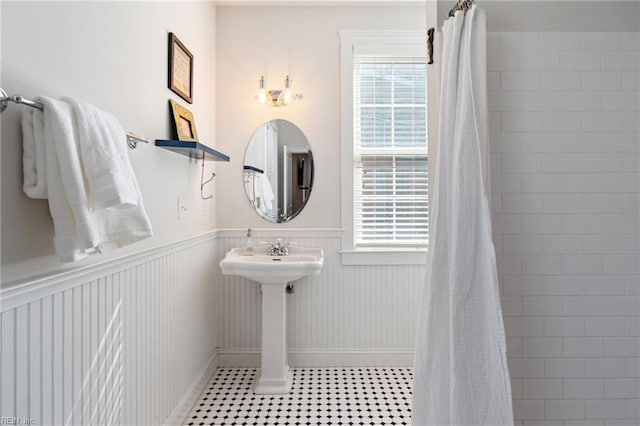 bathroom with a wainscoted wall, tile patterned flooring, a tile shower, and a wealth of natural light