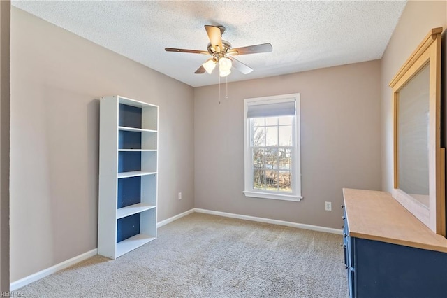 interior space featuring a textured ceiling, a ceiling fan, baseboards, and light carpet