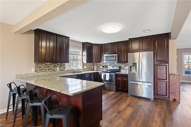 kitchen with dark wood-type flooring, tasteful backsplash, appliances with stainless steel finishes, and a peninsula