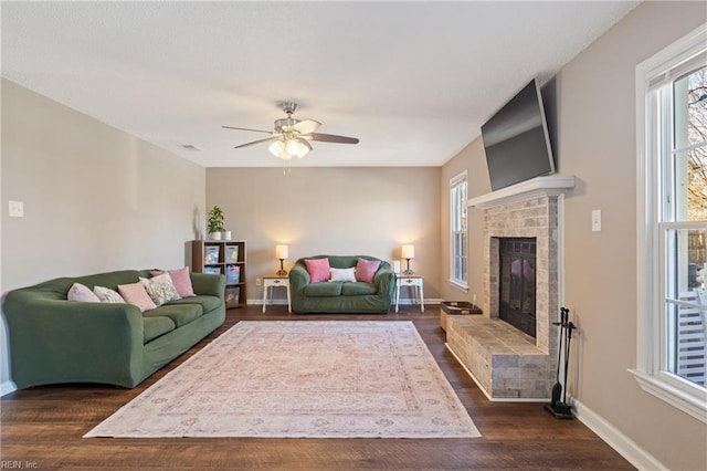 living area with ceiling fan, baseboards, a brick fireplace, and wood finished floors