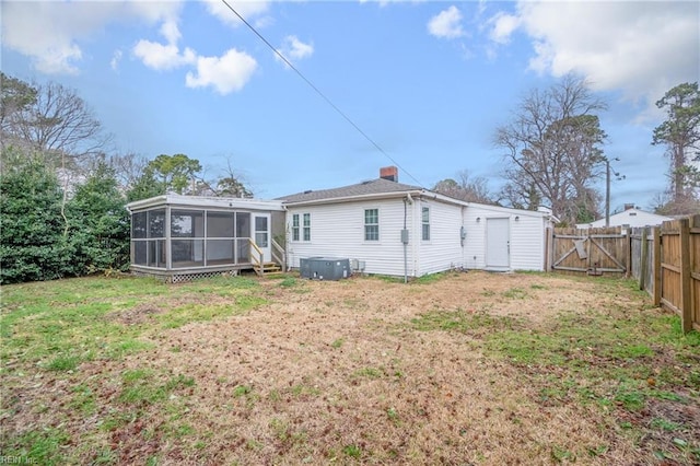 back of house with a fenced backyard, a sunroom, a yard, a gate, and a chimney