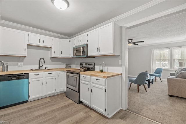 kitchen with appliances with stainless steel finishes, butcher block countertops, a sink, and ornamental molding