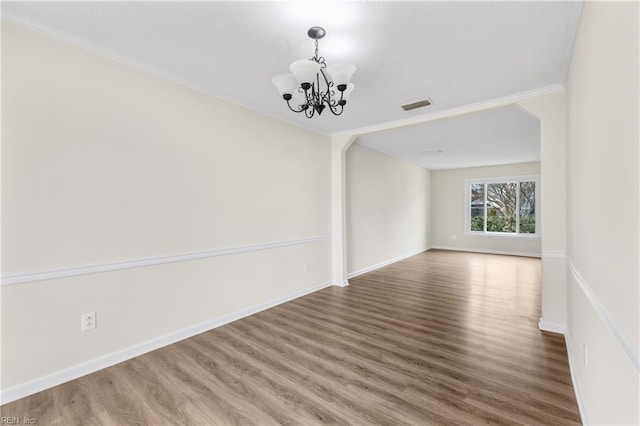 empty room featuring wood finished floors, visible vents, baseboards, and an inviting chandelier