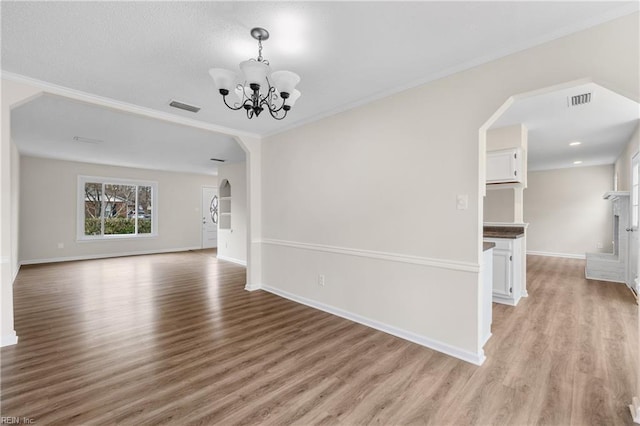 empty room featuring light wood finished floors, visible vents, and arched walkways