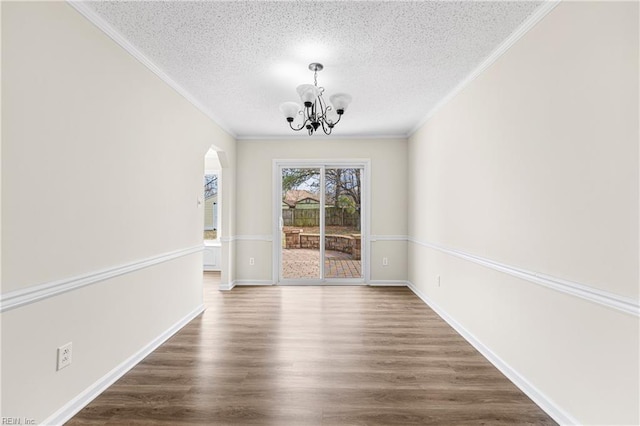 unfurnished dining area with arched walkways, a textured ceiling, a notable chandelier, dark wood finished floors, and crown molding