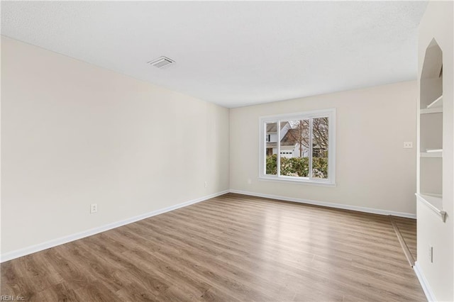 empty room featuring visible vents, baseboards, and wood finished floors