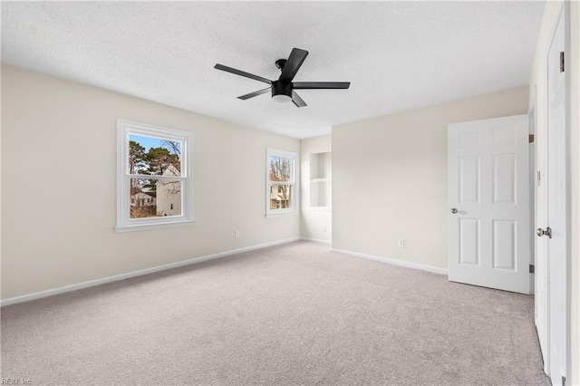 empty room with a ceiling fan, light carpet, a textured ceiling, and baseboards