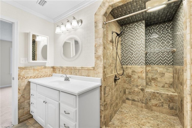 bathroom with visible vents, tiled shower, crown molding, vanity, and tile walls