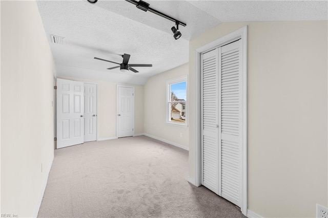 unfurnished bedroom featuring a textured ceiling, carpet flooring, visible vents, baseboards, and rail lighting